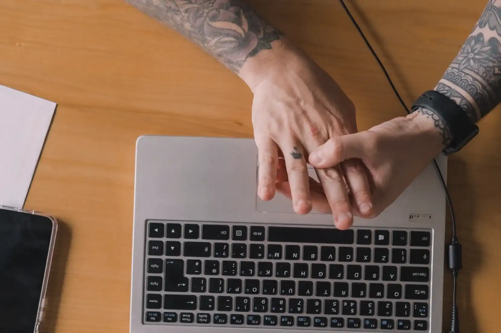 Man with tattoes hands sitting besides the laptop